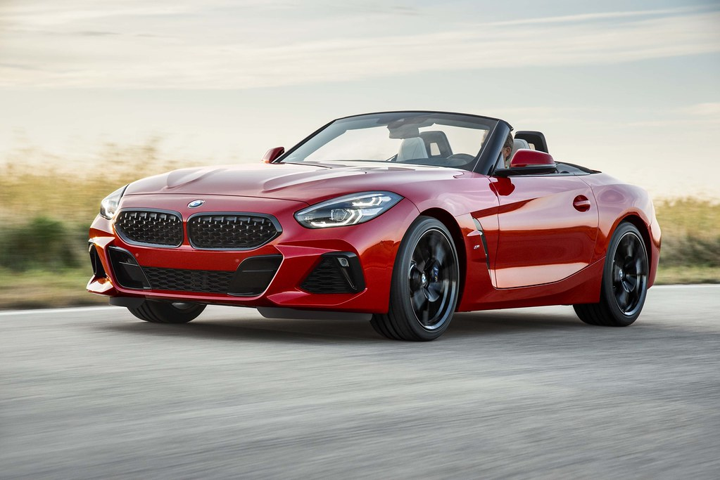The photograph depicts a zippy, red BMW convertible driving quickly down a road.