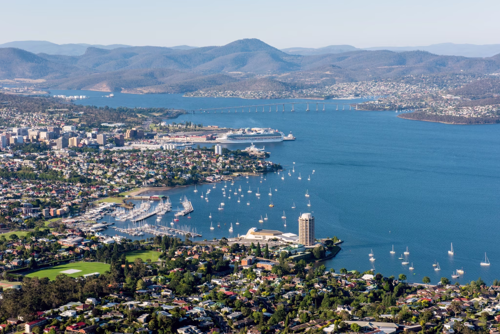 Photo by Alastair Bett for Events Tasmania. An aerial view of Hobart, including the casino, the boats in the harbour, the Tasman bridge, buildings, neighbourhoods, and mountainous landscapes in the background.
