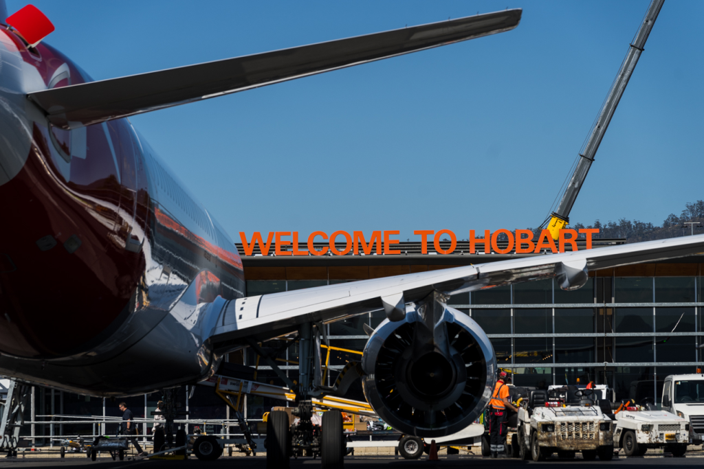 The picture shows the classic "Welcome to Hobart" sign that greets travellers landing at the Hobart Airport. In the foreground, there is a plane wing and engine. This is one of Drive Car Hire's main locations.