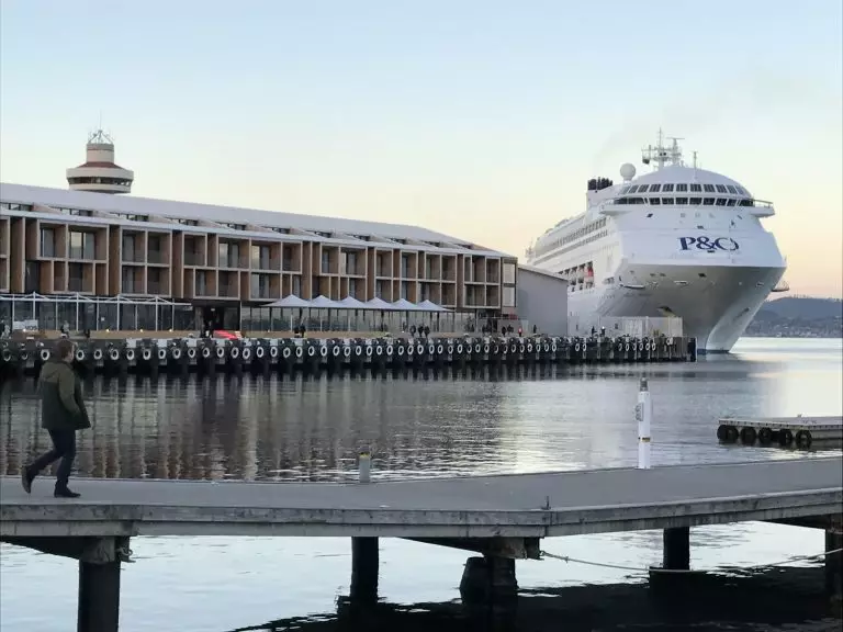 This is a photograph of a bridge, a cruise ship, and a waterfront establishment in Hobart, Tasmania. A person is walking on the left side.