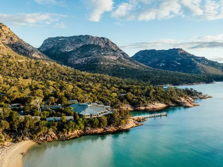 A gorgeous waterside view - turquoise water, a large lodge accommodation overlooking, and a majestic mountain range in the background.