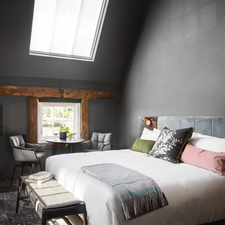 A hotel suite depicted. The room is largely grey with some accented exposed wood and colourful pillows.