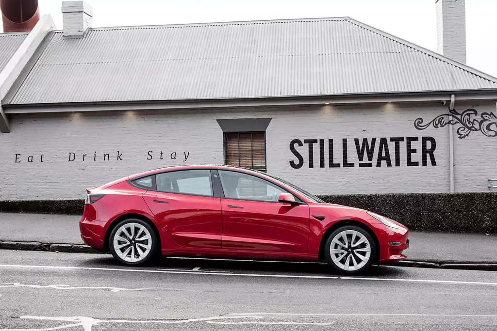 A red Tesla stands in front of Stillwater's "Eat Drink Stay" signage on the side of a white, branded, painted building in Launceston, TAS.