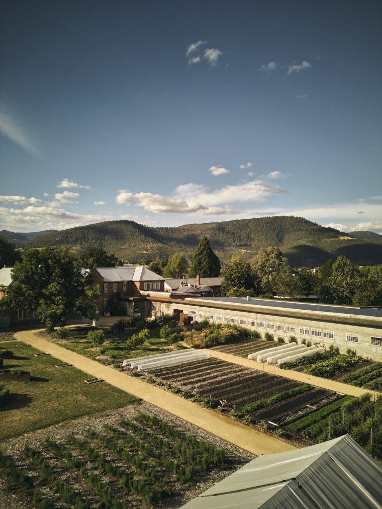 Taken by Luke Burgess, this is an aerial shot of The Agrarian Kitchen depicting the garden, the restaurant, and beautiful hills in the background.