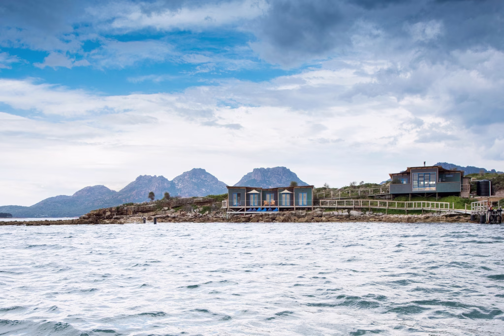 Photographed by Aaron Jones. This is a photo of the water in the foreground with Picnic Island's accommodation and the Hazards mountains in the background.