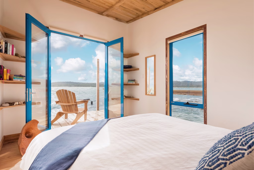 Picnic Island's accommodation is featured in this photo, with a bed, balcony, outdoor chair, and beautiful, serene ocean scape view. Photo credits to Aaron Jones.