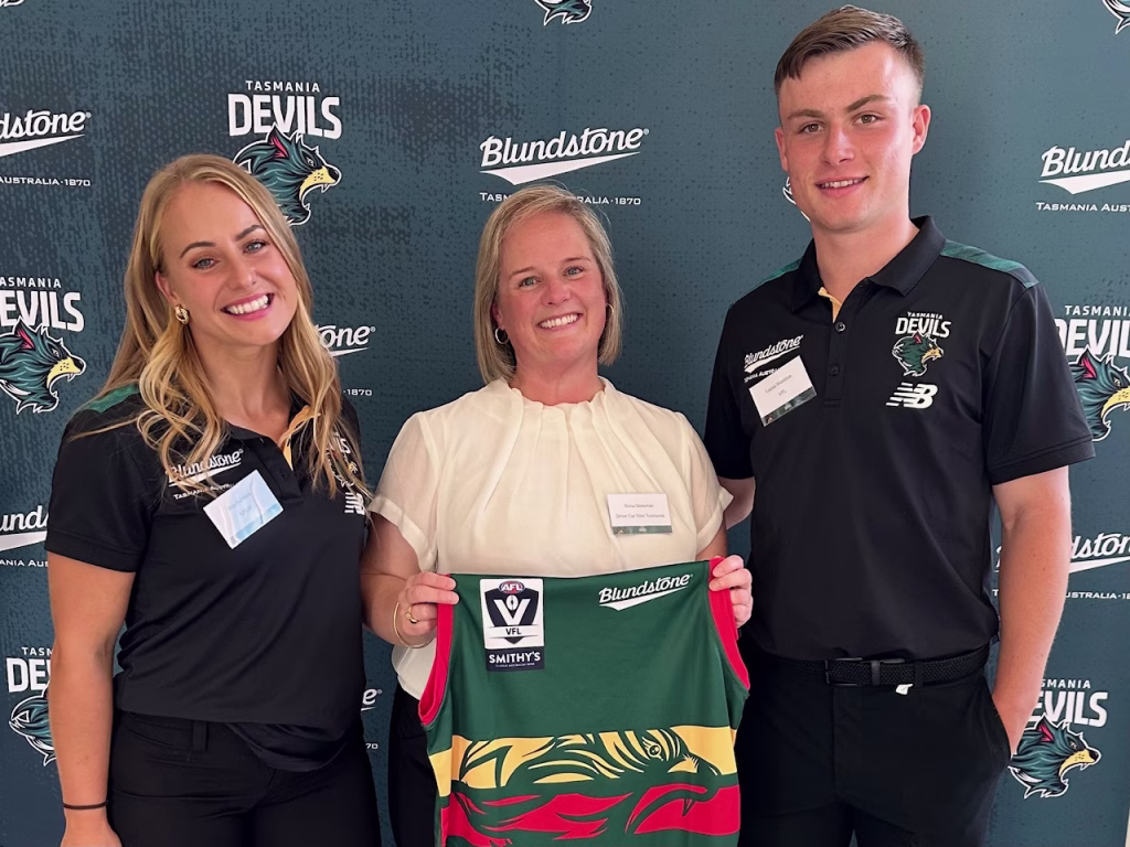 Drive Car Hire general manager Anna Donovan stands between Tasmanian football players Brie Barwick (right) and Lucas Wootton (left). She holds a green Tasmania Devils jersey in hand.