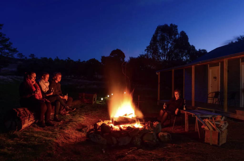 Four people sit with a dark blue sky around a fire enjoying an evening at Rathmore.