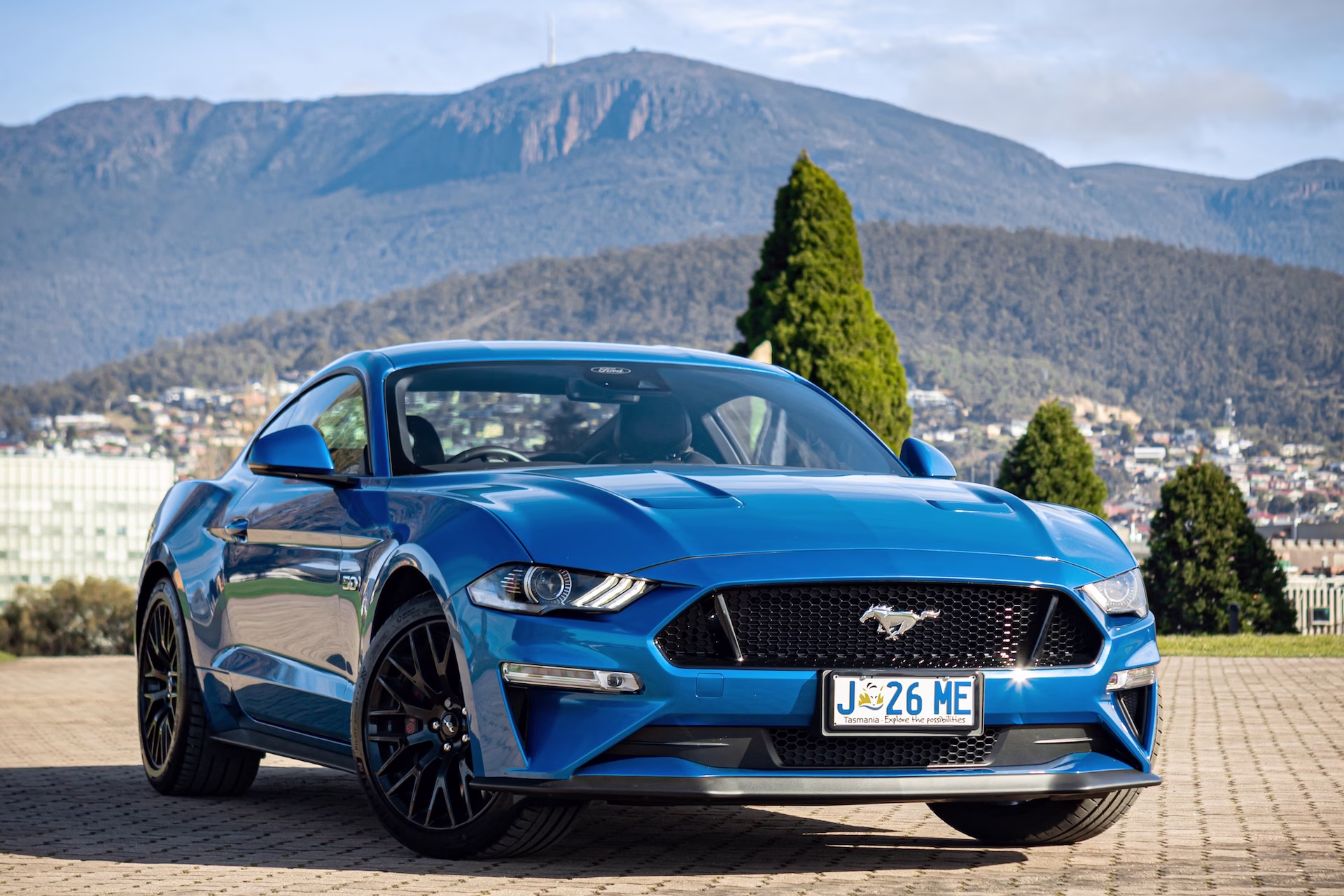 Drive Car Hire Hobart City Information. A blue Mustang stands parked in front of Hobart landmark kunanyi / Mount Wellington.