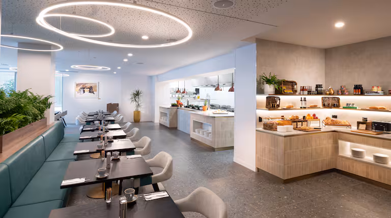 The breakfast buffet at Leatherwood Bar & Kitchen in Hobart is featured in this shot. There is a row of small tables, an open kitchen area, and some foods and sauces laid out.