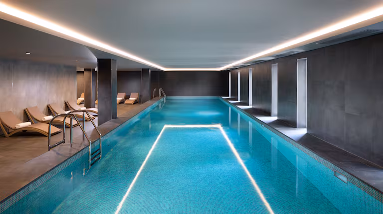 The indoor pool at the DoubleTree Hilton in Hobart, Tasmania. A few pool chairs are off to the left side, and the rectangular pool is a bright turquoise shade with light reflected into the water.