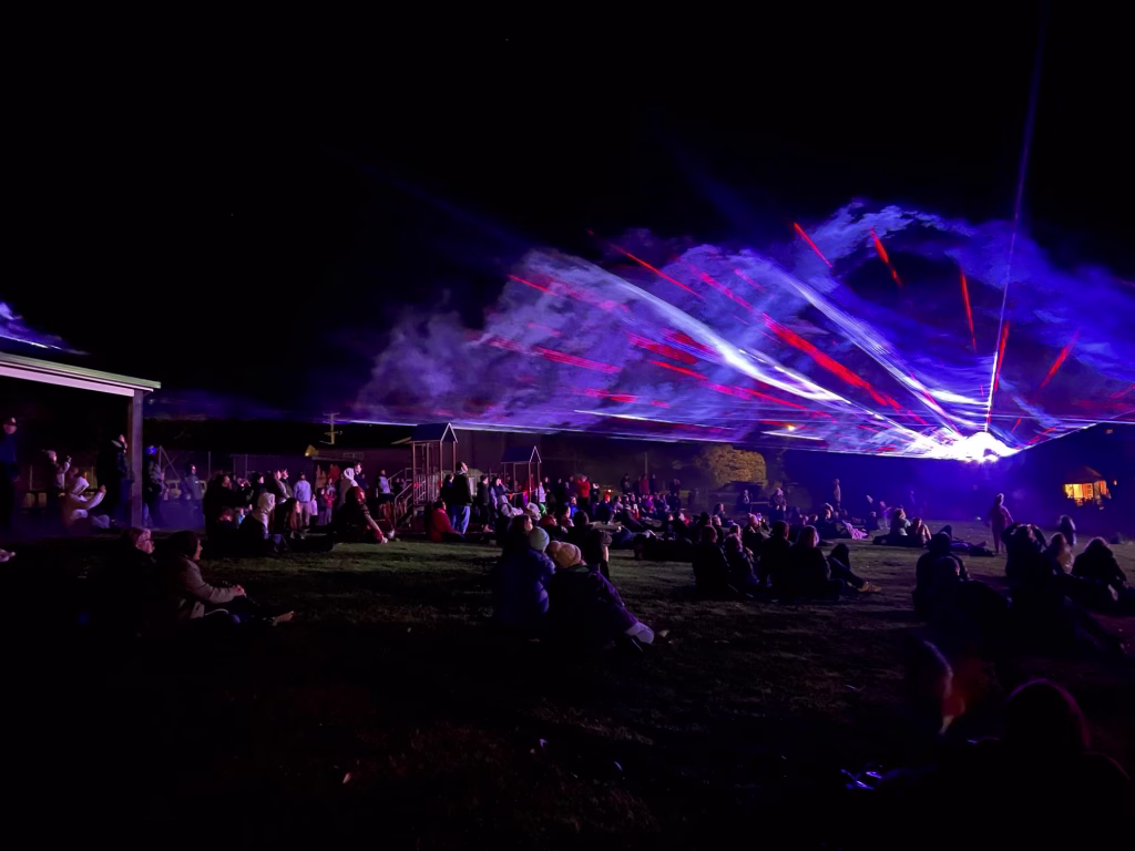 A group of people sit on the ground in front of a light show at the Bicheno Beams.

Photographer: K. Poole