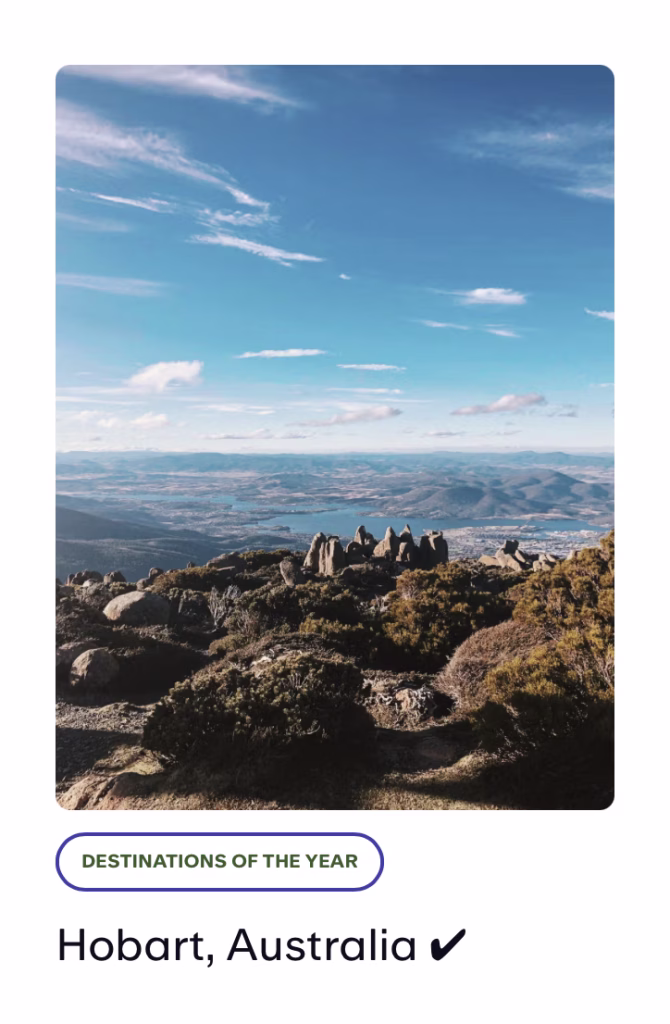 A photo of Mt. Wellington in Hobart, Australia. Under the expansive nature shot picturing rocks, flora, lakes, and mountains, we see the text "Destinations of the year" and "Hobart, Australia" with a check mark.